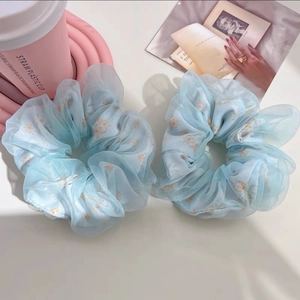 Vue détaillée de deux chouchous en organza bleu clair avec imprimé de marguerites oranges