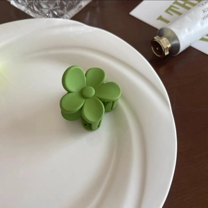 Détail d'une petite pince à cheveux fleur verte mate sur une assiette en céramique