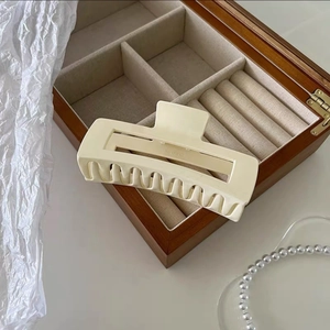 Detail view of a large cream matte hair claw clip on a wooden jewelry box with pearls
