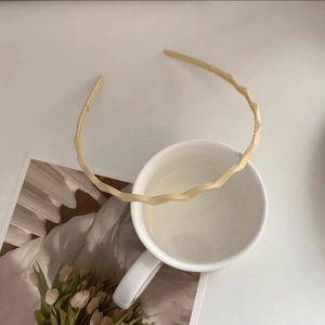 Detail shot of a candy-colored wavy headband in beige resting on a white ceramic mug