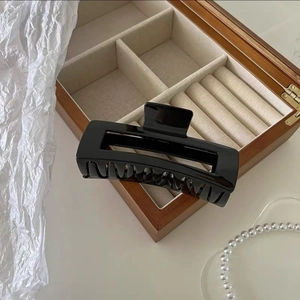 Macro shot of 12.5cm large black claw clip with hollow rectangular design on a wood box
