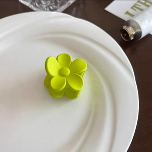 Détail macro d'une pince à cheveux fleur mate vert néon sur une assiette en céramique