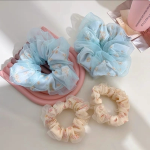 Détail de quatre chouchous en organza à fleurs sur un plateau décoratif rose