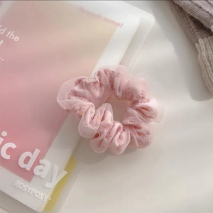 Détail d'un chouchou en résille rose clair avec imprimé marguerites sur tissu doux voile