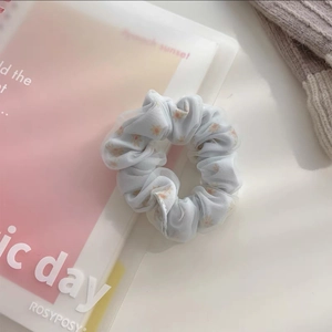 Détail d'un chouchou en tulle bleu clair avec motif marguerite sur fond rose et beige