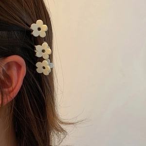 Detailed close-up of three cream flower hair claws used for styling on long brown hair