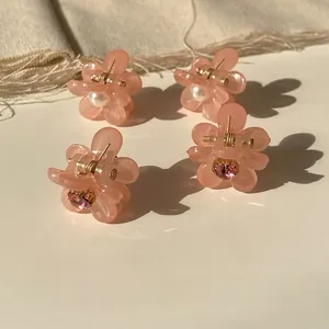 Dettaglio di quattro mini mollette per capelli a fiori in acrilico rosa con perline