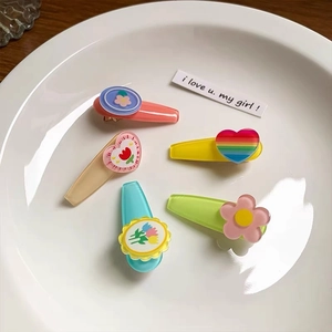 Close-up of five colorful resin hair clips with tulip and daisy icons on a white plate