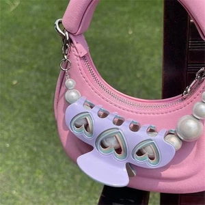 Détail d'une pince à cheveux cœur violette sur la anse d'un sac rose