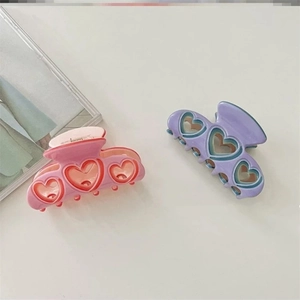 Détail de deux grandes pinces à cheveux coeur évidé en résine rose-orange et violet-vert