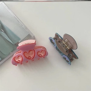 Détail de pinces à cheveux en forme de cœur rose et violet sur fond blanc minimaliste