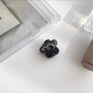 Macro detail of mini black resin flower hair clip with white marble texture finish