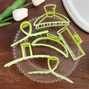 Set of five elegant green metal hair claws in various geometric shapes on a tray