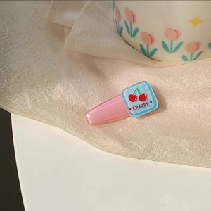 Detail of pink acrylic hair clip with a blue block featuring a cherry and text