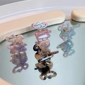 Mini butterfly hair claws in colorful gradient resin with reflections on a mirror surface