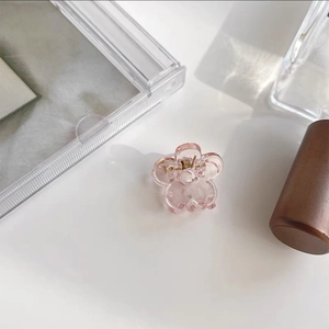 Close-up of a mini pink flower hair claw clip with golden spring on a clean white desk
