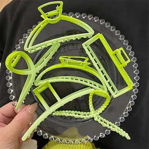 Detail view of five neon green matte hair claws in various shapes on a glass tray