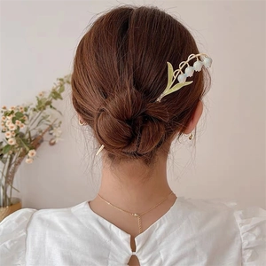 Gros plan d'un pic à cheveux muguet doré avec bourgeons blancs sur un chignon élégant
