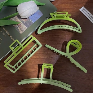 Set of four light green matte hair claws in geometric shapes on a wooden desk
