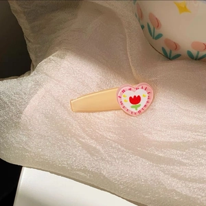 Close-up of heart-shaped hair clip featuring a red tulip motif on white fabric