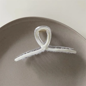 Detail shot of a minimalist acrylic hair claw clip with golden metal spring on a tray