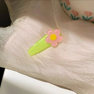 Close-up of pink flower resin hair clip with green duckbill base on white silk