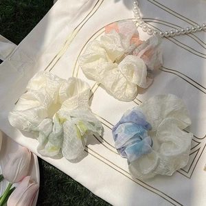 Three organza scrunchies in pastel colors on a canvas bag with flowers and pearls