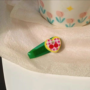 Detailed view of green cherry pattern hair clip on a decorative white porcelain cup