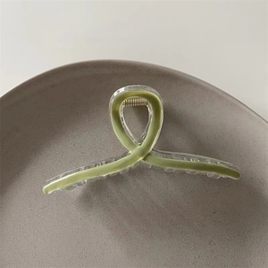 Macro detail of avocado green acrylic claw clip with cross twisted design on grey plate