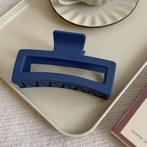 Macro shot of matte dark blue 12cm hair claw clip on a stylish ceramic tray