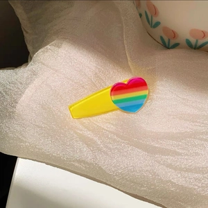 Close-up of yellow acrylic hair clip featuring a colorful rainbow heart ornament