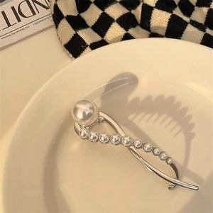 Detail van een zilveren haarklem met elegante parels in een kriskras ontwerp