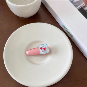 Detailed close-up of a pink resin hair clip featuring a cherry design on a ceramic plate