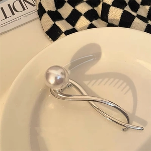 Detailweergave van zilveren haarklem met grote glanzende parel op een minimalistische golfband