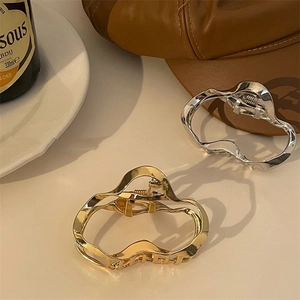 Detailed view of gold and silver irregular wave metal hair claws on a beige table