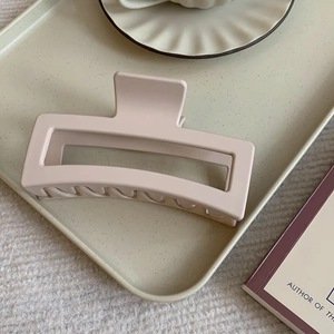 Detail of matte cream-pink rectangular hair claw clip on a decorative beige tray