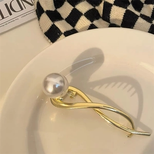 Detailopname van een gouden metalen haarklem met een grote parel in een witte schaal