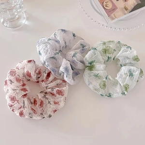Détail de trois chouchous à fleurs rouge, bleu et vert sur une table blanche