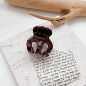 Detail view of a glossy dark brown mini hair claw clip on marble and wooden background