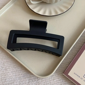 Macro shot of a matte black 12cm oversized hair claw clip on a stylish beige tray
