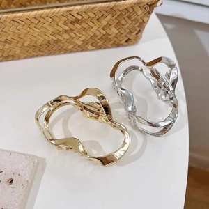 Detail of gold and silver geometric irregular wave metal hair clips on a minimalist surface