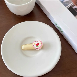 Close-up of a cream tulip heart hair clip on a white ceramic plate with a wooden background