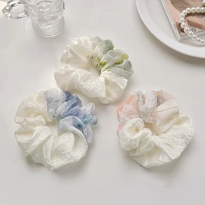 Close-up of three pleated organza scrunchies in pastel prints with aesthetic props