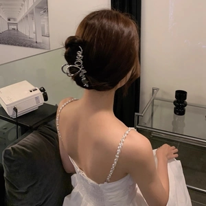 Detail view of a silver LOVE metal hair claw clip with elegant pearls on a hair bun