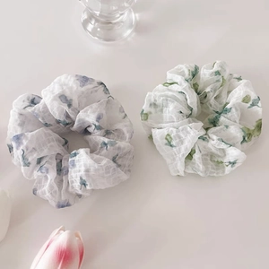 Détail d'un lot de chouchous à fleurs aux motifs bleus et verts sur un tissu transparent