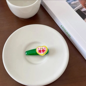 Detail of candy-colored green hair clip with heart cherry pattern on a ceramic dish