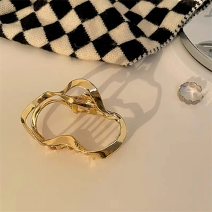 Detail shot of wavy gold-plated metal hair claw clip on a checkered pattern backdrop
