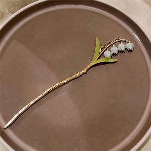 Détail d'épingle à cheveux muguet avec feuilles vertes et fleurs blanches sur tige dorée