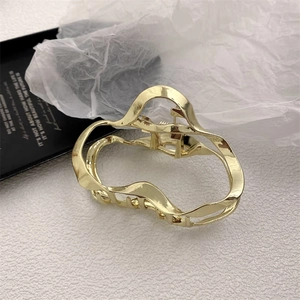 Macro view of a polished gold irregular wave metal hair claw clip on a white background