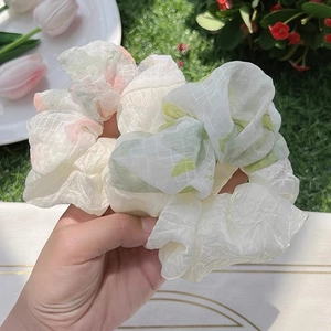 Pastel organza scrunchies with floral and grid patterns on a fresh grass background